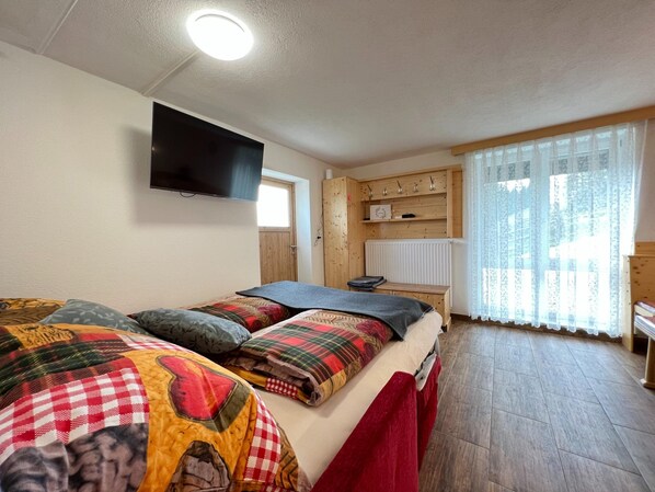 A bedroom with a bed, a TV mounted on the wall, a wooden cabinet, and a window with curtains. - Alpine House in Prebl Near Klippitztorl Ski Area (Wolfsberg)