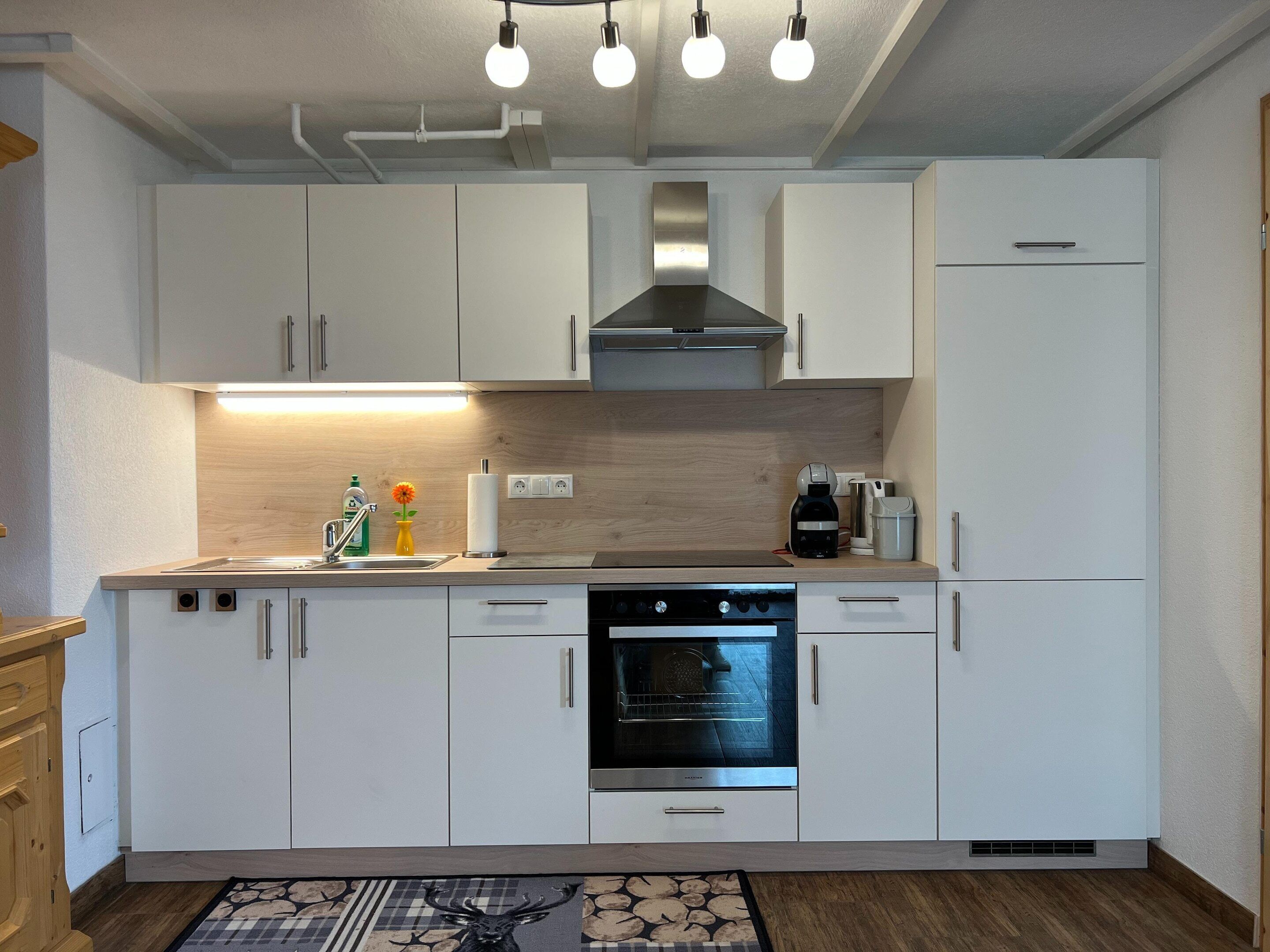 A modern kitchen with white cabinets, a built-in oven, and a coffee maker.