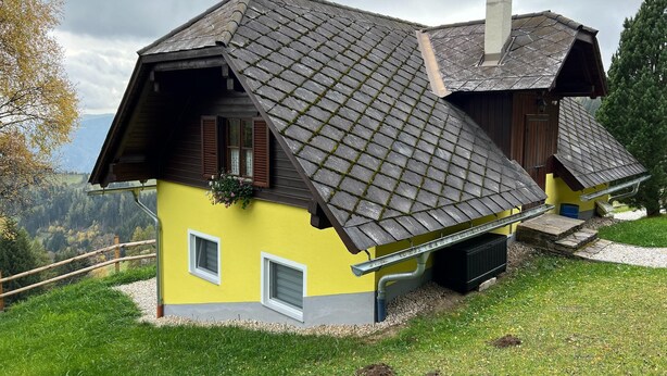 Une maison avec un toit à forte pente, une cheminée et une fenêtre avec des volets.