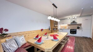 Une cuisine compacte avec des meubles blancs, une table à manger en bois agrémentée de serviettes rouges et un banc avec des coussins à motifs.