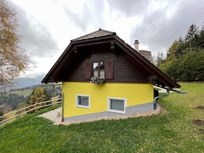 Ein gelbes Gebäude mit braunem Dach, zwei Fenstern und einem Schornstein.