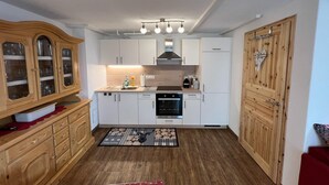 Une cuisine compacte avec des meubles blancs, un meuble en bois doté de portes en verre, un four encastré et un four à micro-ondes.