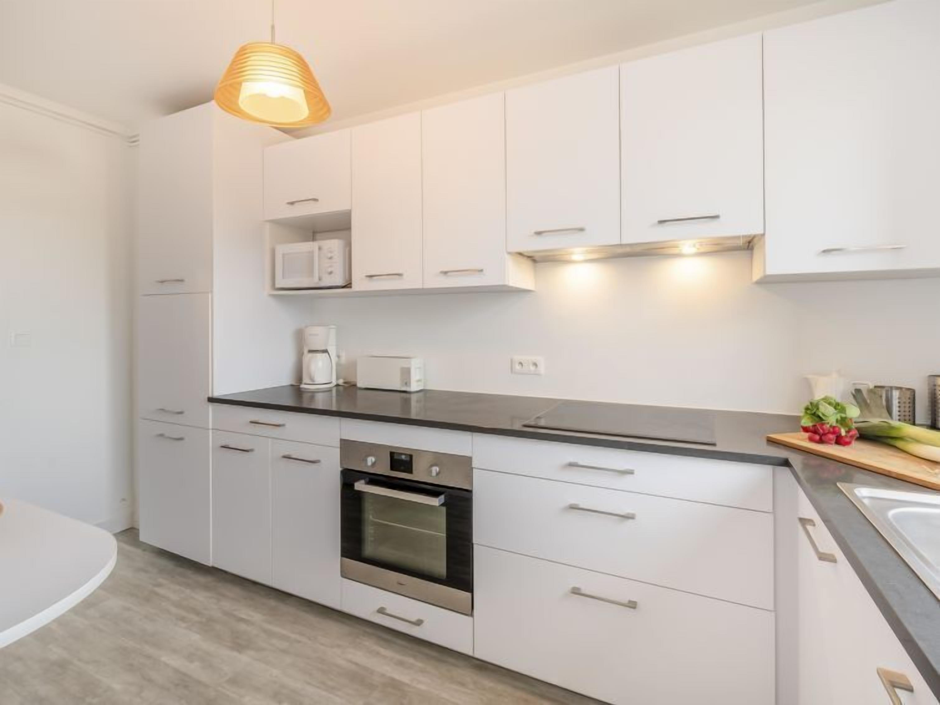 Una cocina moderna con armarios blancos, horno empotrado, microondas y cafetera.