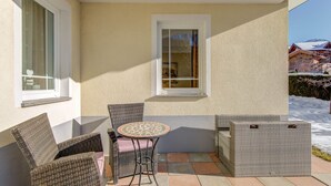 A patio with wicker furniture and a tiled floor, a window with a view of a snowy landscape, and a building with a beige exterior. - Inviting Apartment in Fiss in the Mountains (Fiss)