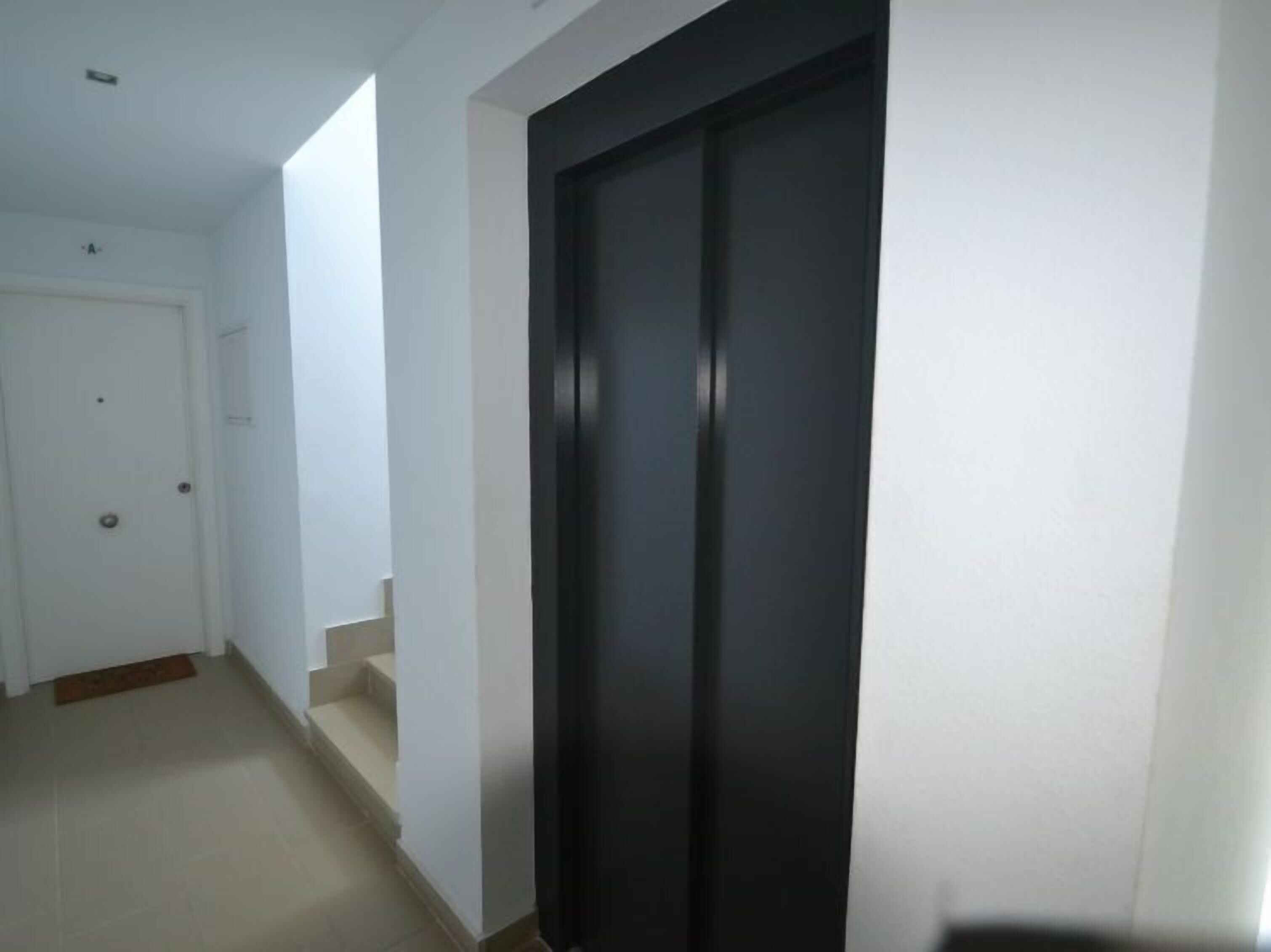 A hallway with a black door, white walls, and a tiled floor.