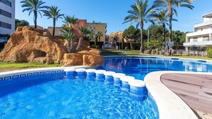 A swimming pool with clear blue water, surrounded by palm trees and a rocky formation. - Tramontana by Interhome (Salou)
