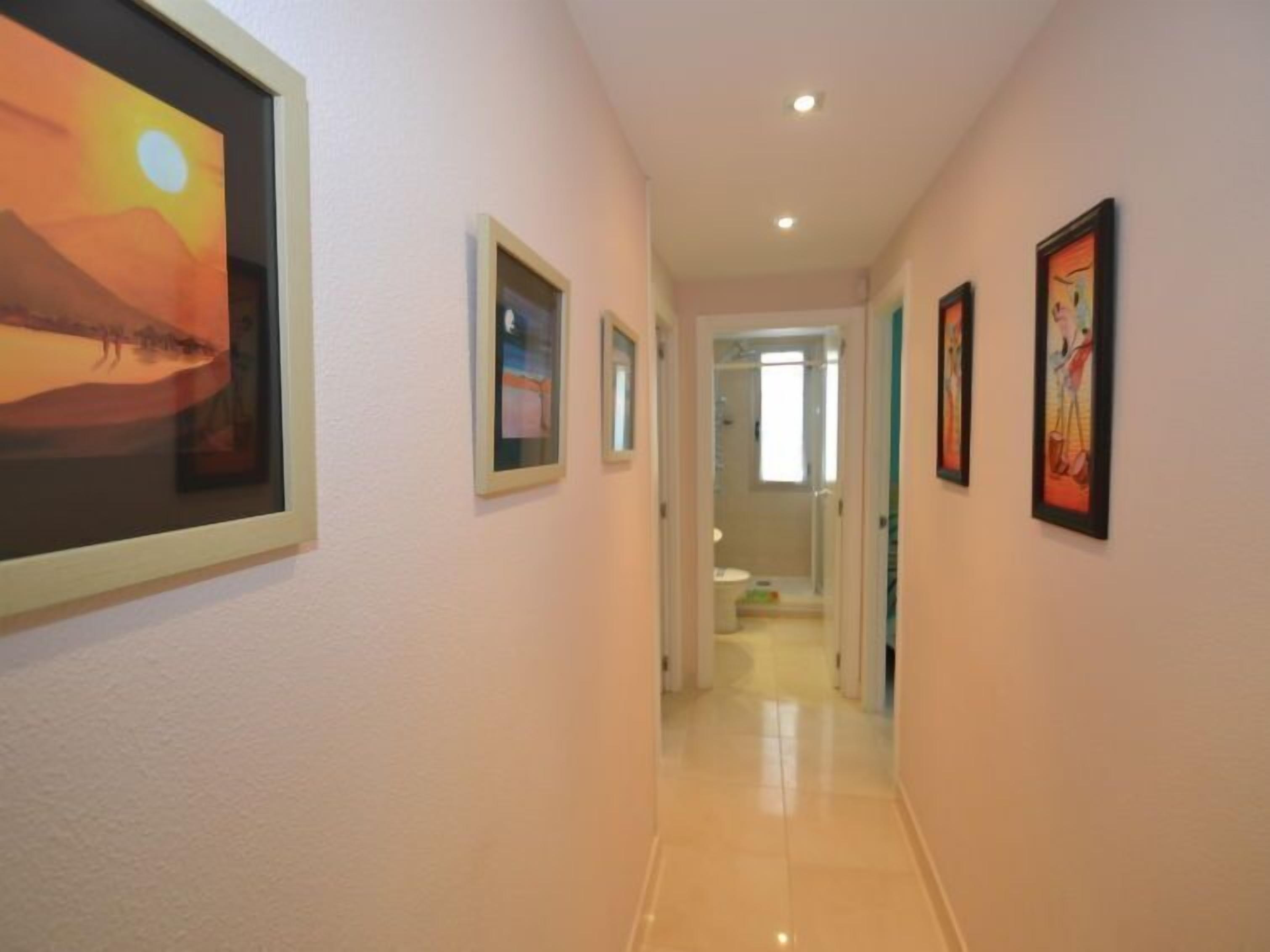 A hallway with framed artwork on the walls, leading to a bathroom.