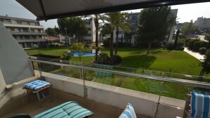 A balcony with a view of a well-maintained lawn, palm trees, and a building in the background. - Tramontana by Interhome (Salou)