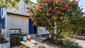 A patio with a grill, picnic table, and a tree with red flowers. - La Perle by Interhome (Cancale)
