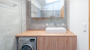 Une salle de bain moderne avec un meuble-lavabo en bois, un lave-linge encastré et un grand miroir.