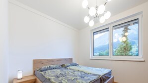 Une chambre avec un lit en bois, une table de chevet, une lampe fixée au mur et une fenêtre donnant sur la montagne.