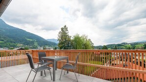 Un balcon avec une table et des chaises, d’où l’on peut admirer un paysage montagneux.