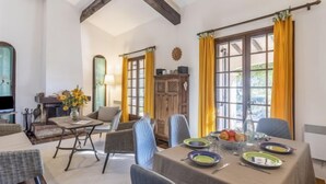 Un coin repas avec une table dressée pour quatre personnes, entouré de chaises en osier, d’un meuble en bois et d’un téléviseur.