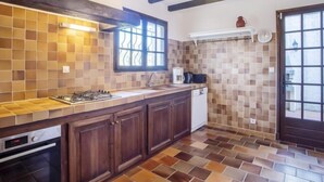 Une cuisine équipée d’une cuisinière à gaz, d’un four et d’un lave-vaisselle. Elle comprend une fenêtre avec vue, un luminaire suspendu et une porte avec un vitrage.