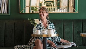 A woman sitting on a green upholstered bench in a room with a green wall and a large mirror reflecting the interior. - Hotel La Gemma (Florence)