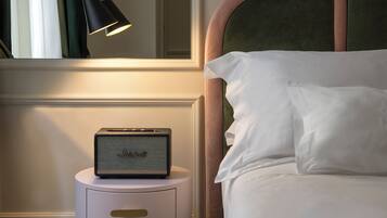 A neatly made bed with white linens, a small bedside table with a lamp, and a Marshall speaker.
