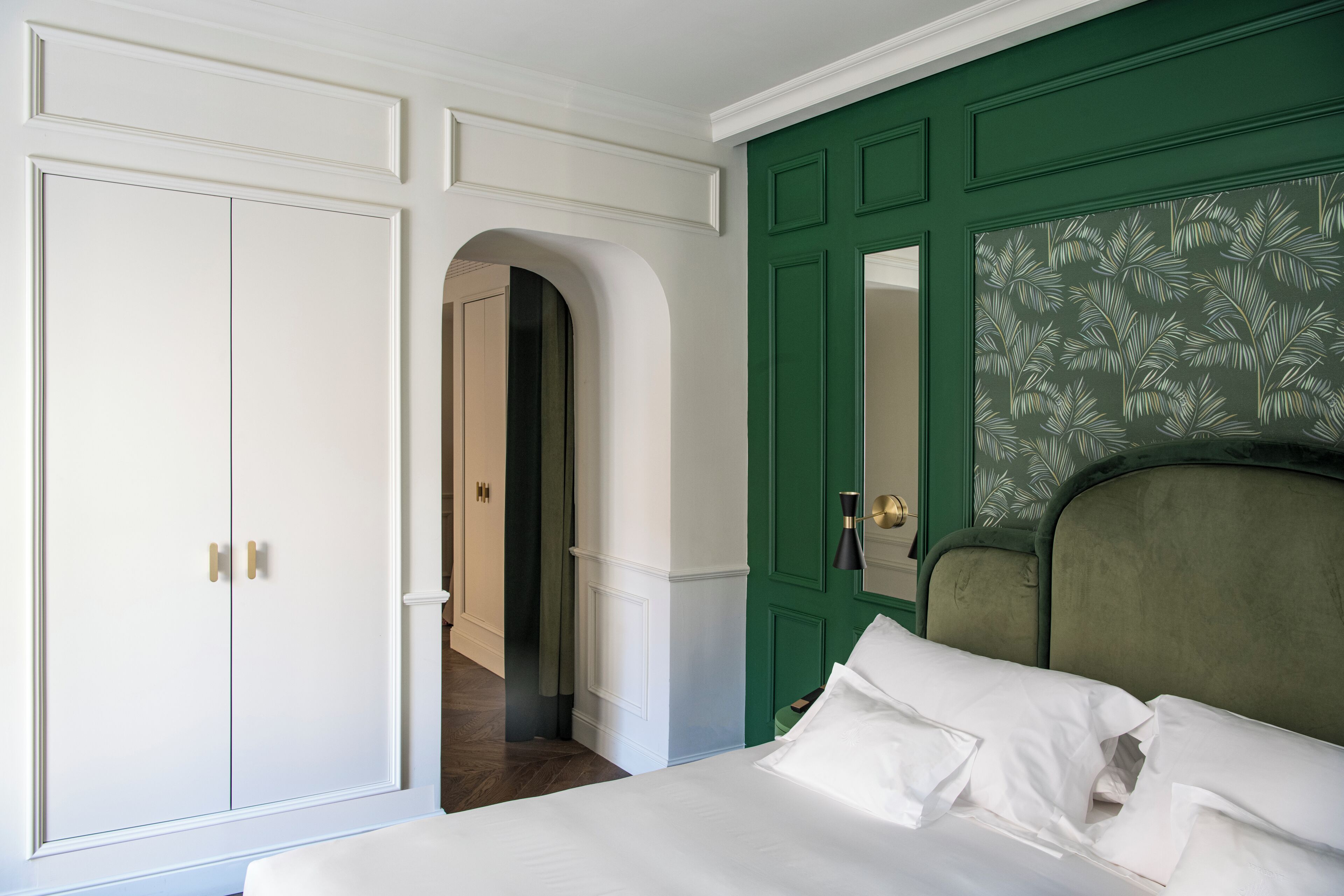 A bedroom with a bed, a green accent wall, a white wardrobe, and a mirror.