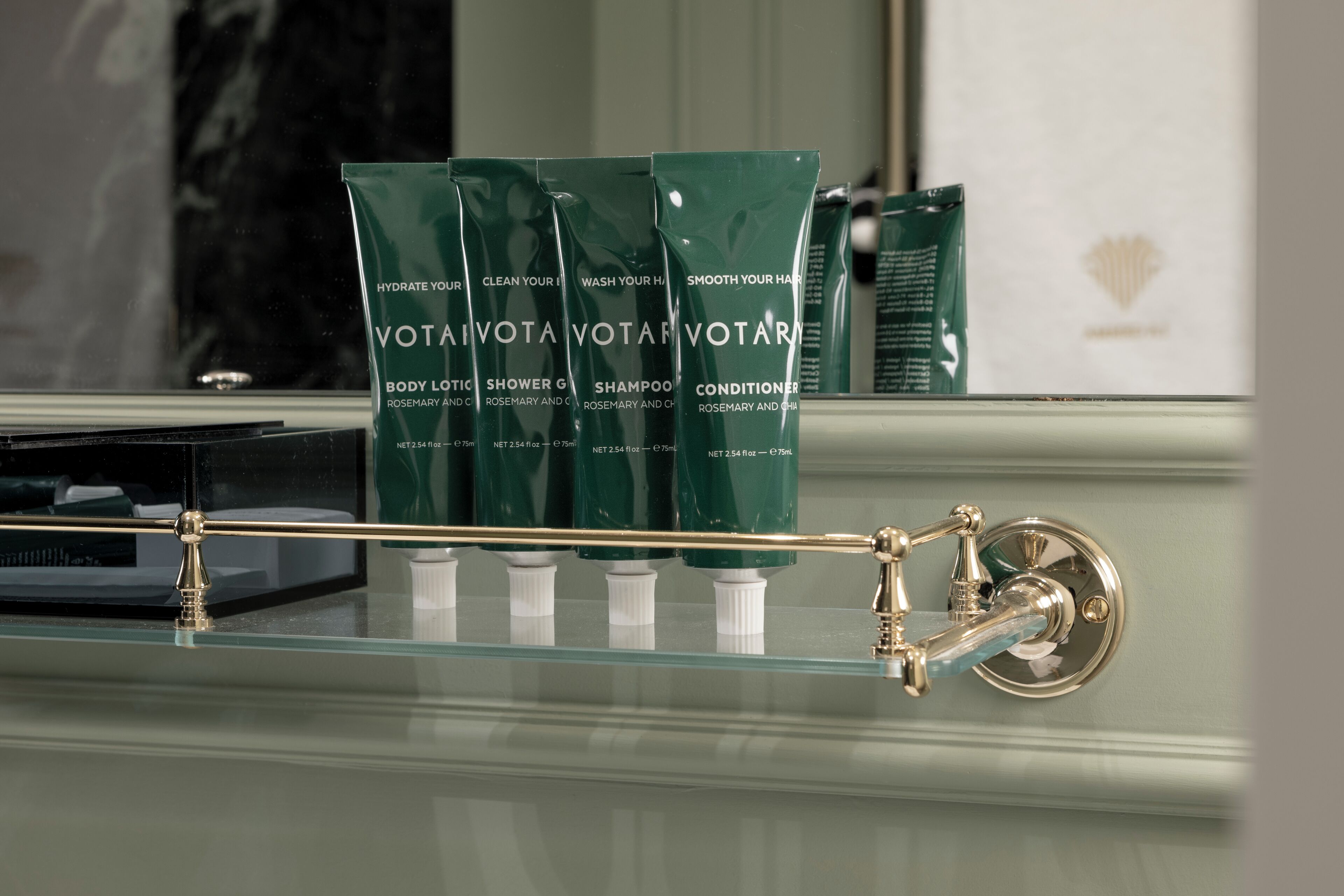 A bathroom with a glass shelf displaying Votava Votare body lotion, shower gel, shampoo, and conditioner.
