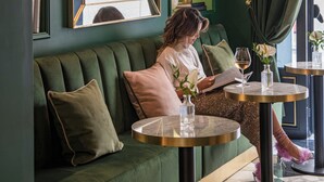 A green upholstered sofa with a mirror, a table with a wine glass, and a lamp. - Hotel La Gemma (Florence)