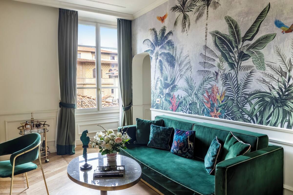 A living room with a green sofa, a round coffee table, a decorative bird statue, and a tropical mural on the wall.