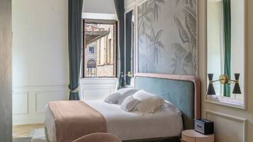 A bedroom with a bed, a nightstand, a chair, a window with curtains, and a view of a building outside.