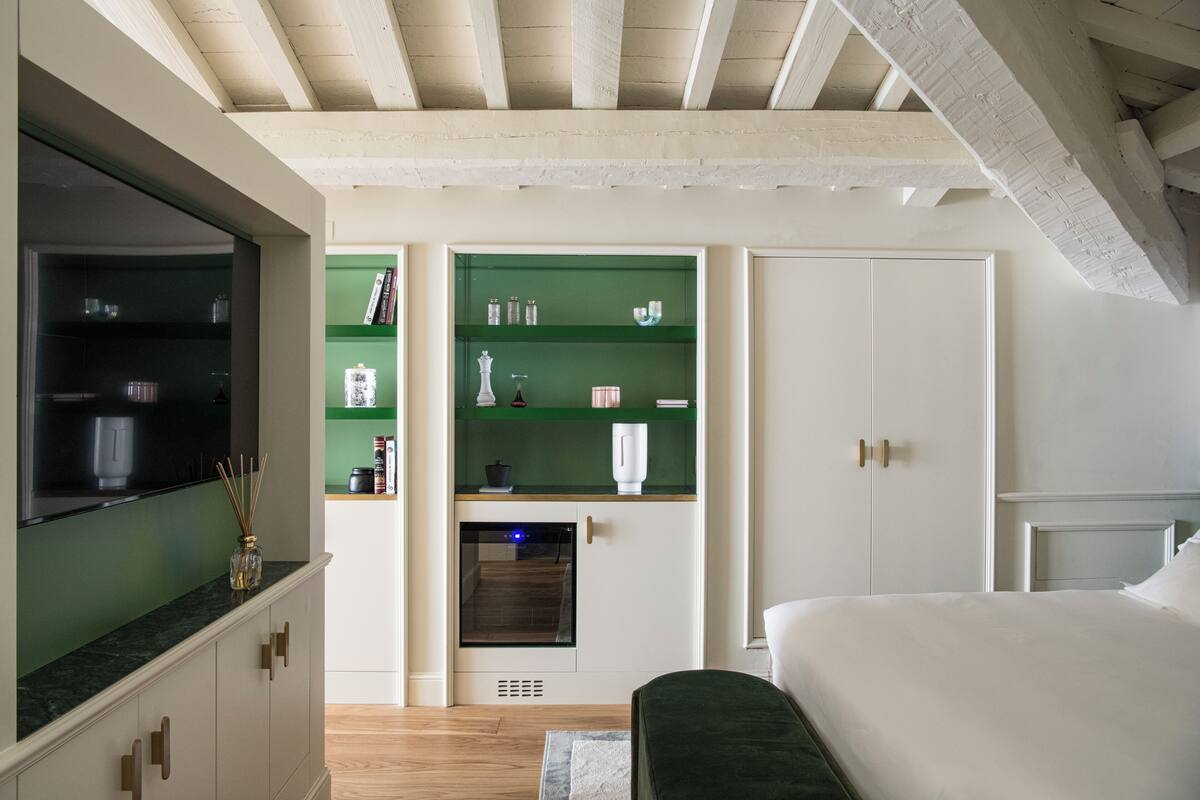 A bedroom with a bed, a wardrobe, and a green shelf unit with kitchen items.