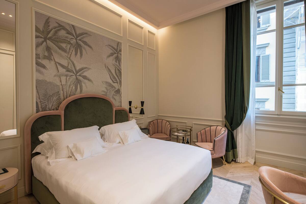 A hotel room with a large bed, a small table, two chairs, and a wall with a palm tree mural.