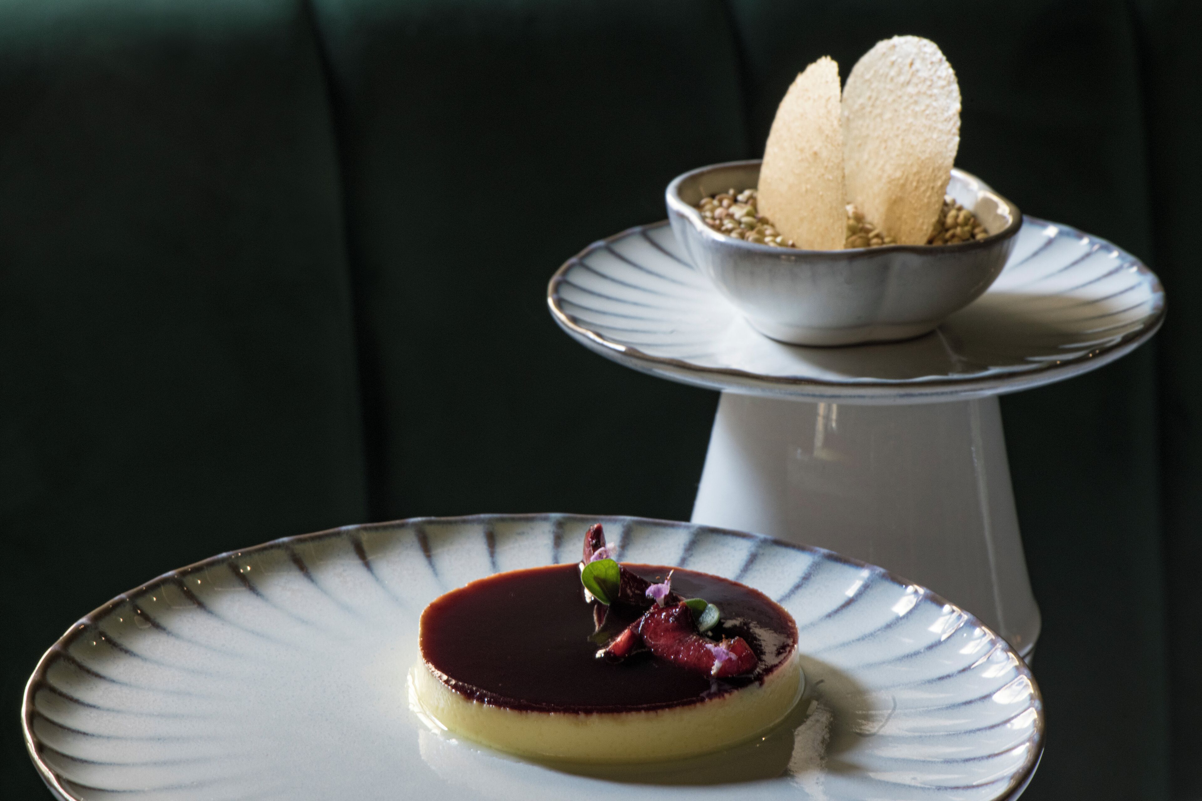 A dessert on a plate with a dark sauce and garnishes, and a bowl with two ice cream cones on a pedestal stand.