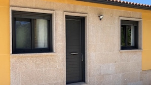 Un edificio con fachada amarilla, una puerta oscura y dos ventanas con cortinas.
