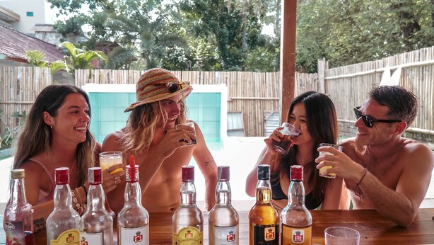 A group of people sitting at an outdoor table with various bottles of alcohol in front of them. - Indonesia Backpacker Hostels  (Kuta)