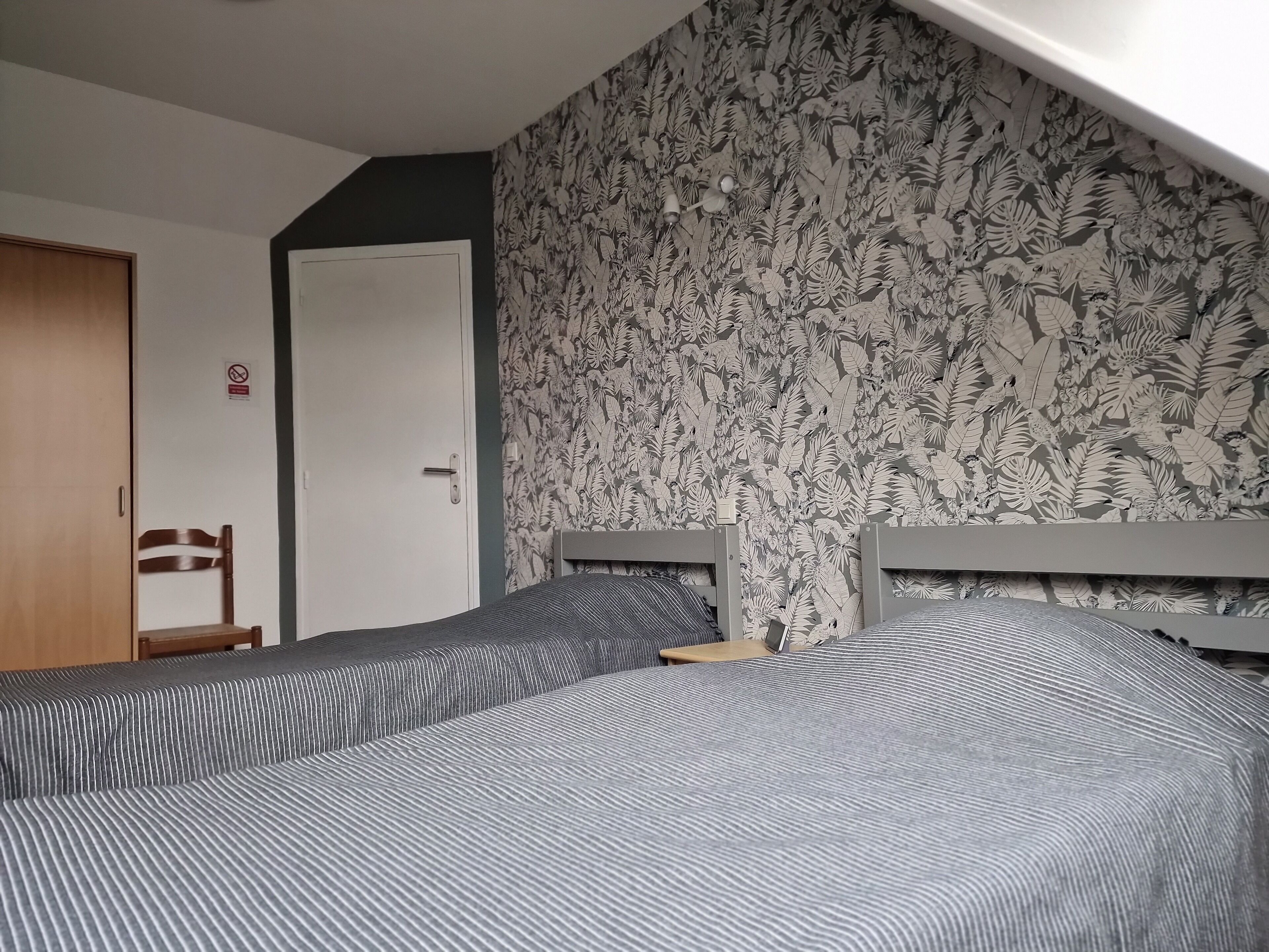 A room with two beds, a wooden chair, a door, and a wall with a leaf pattern.