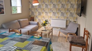 Quarto mobiliado com sofá, cadeira, mesa com um vaso, TV na parede e papel de parede estampado.