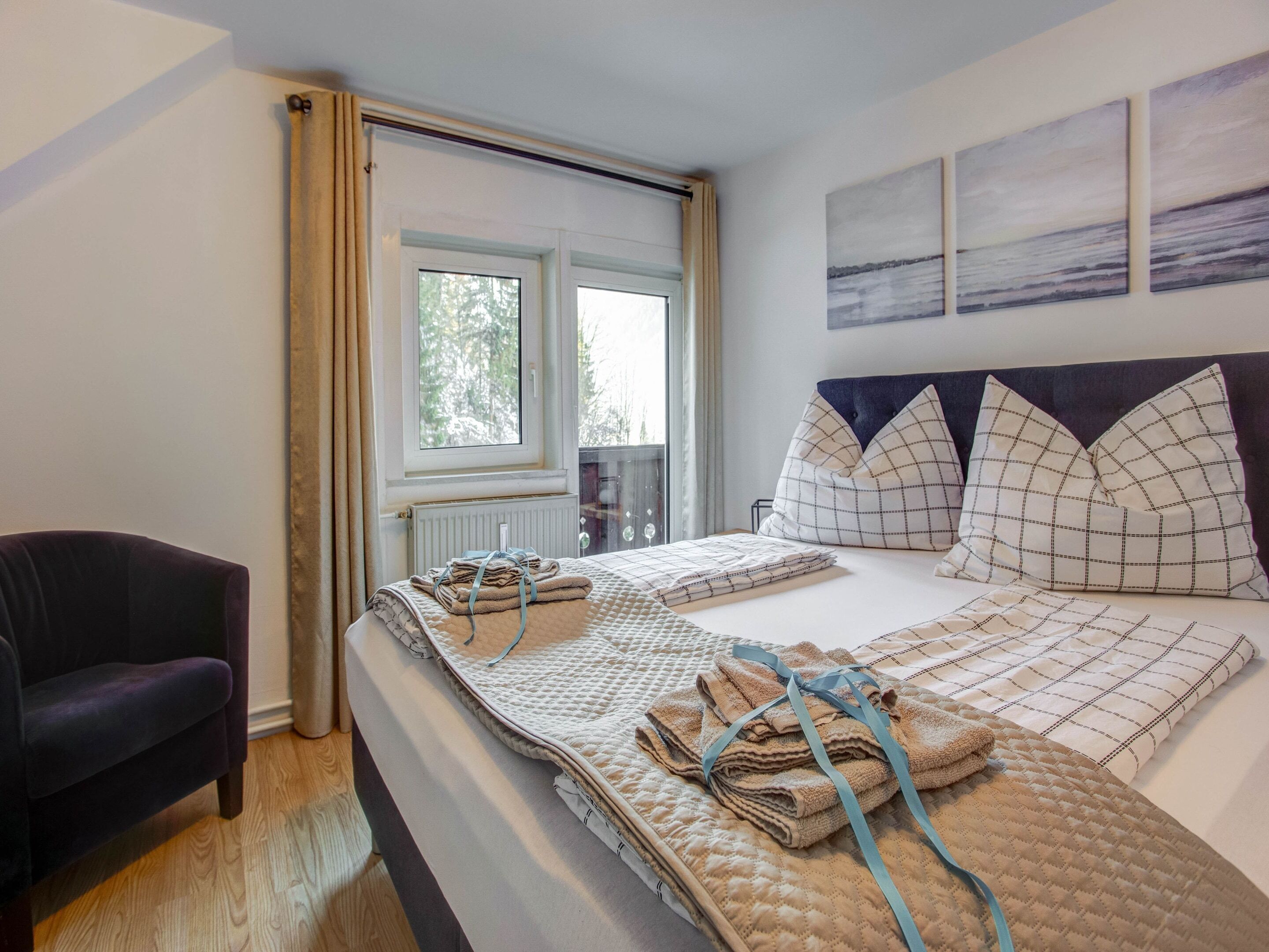 A bedroom with a bed, a chair, a window, and two wall-mounted paintings.