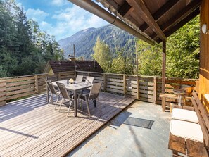 Een houten terras met een tafel en stoelen, met uitzicht op een bebost dal en bergen.