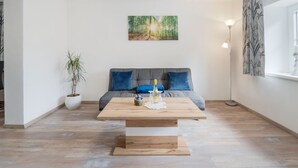 A modern living room with a sofa, a coffee table, a potted plant, and a painting on the wall. - Apartment in Bad Mitterndorf Near ski Area (Bad Mitterndorf)