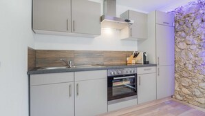 A modern kitchen with grey cabinets, a built-in oven, and a stone accent wall. - Apartment in Bad Mitterndorf Near ski Area (Bad Mitterndorf)