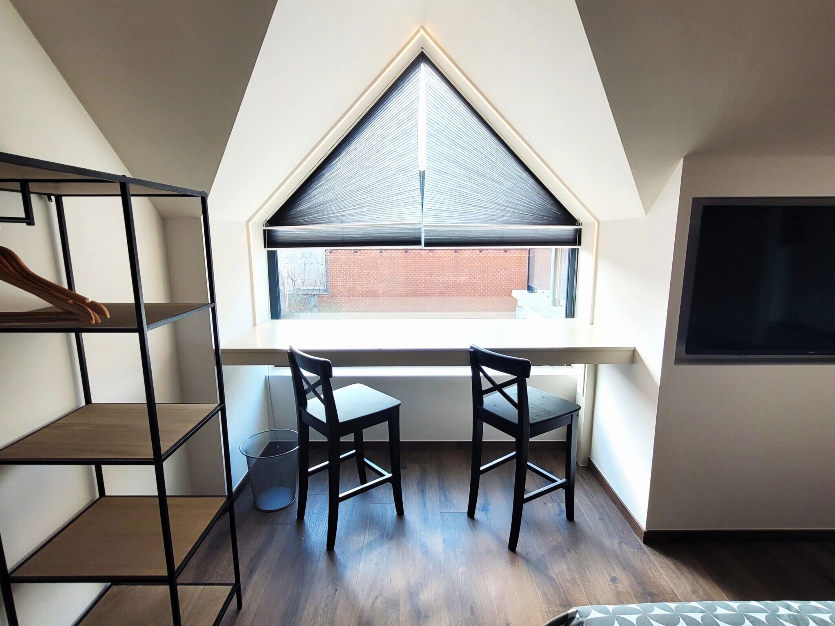 A small, modern room with a sloped ceiling, a large window, two chairs, and a desk.