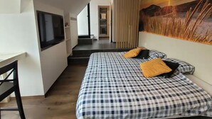 Une chambre d’hôtel moderne avec un lit à motifs à carreaux, une télévision, un bureau et un tableau représentant un coucher de soleil.
