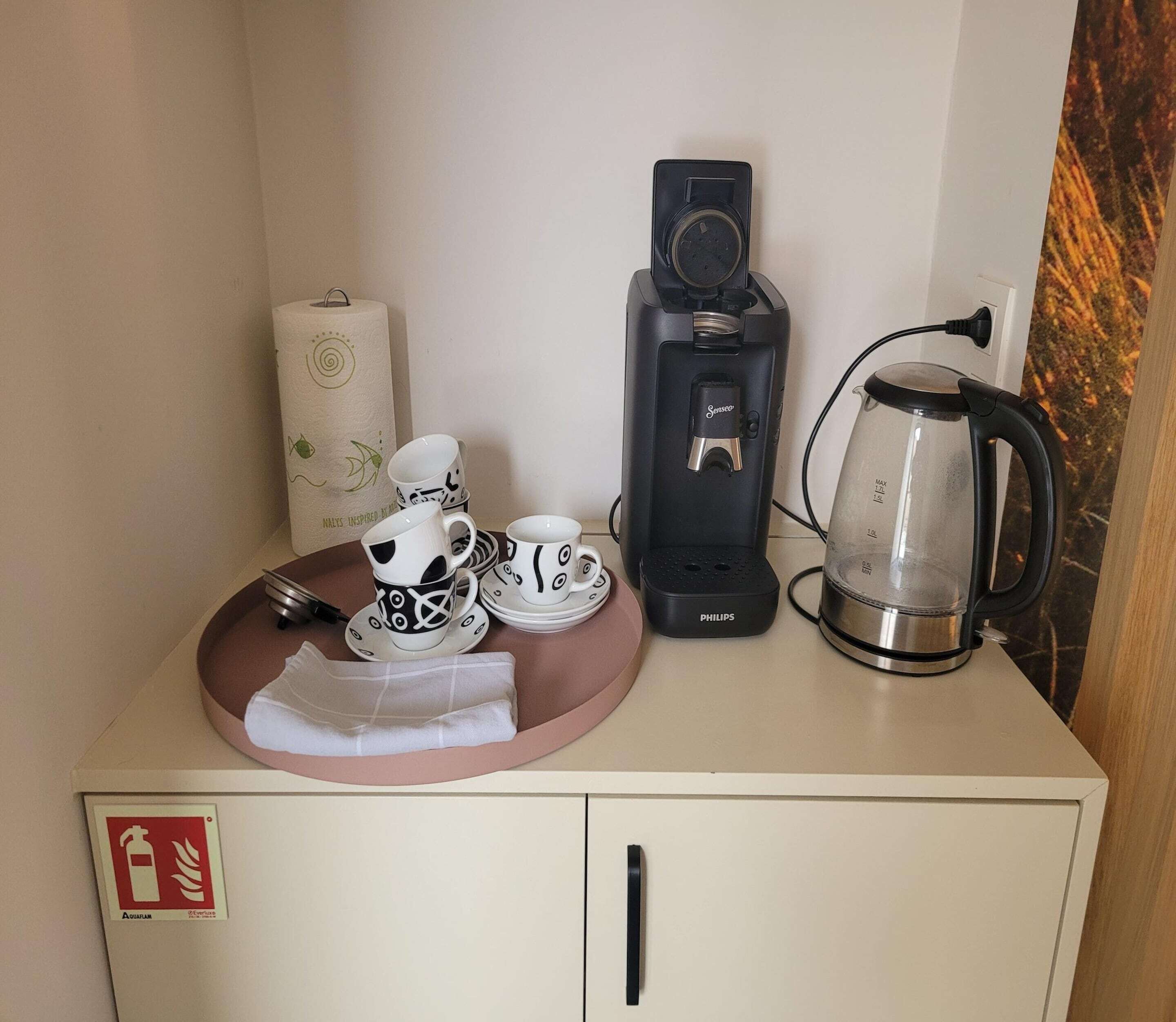 A kitchenette with a coffee maker, a kettle, and a tea set on a counter.