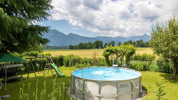 Un patio trasero con una piscina elevada circular, un columpio y un tobogán.