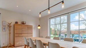 Un comedor moderno con una mesa y sillas de madera, un armario alto y ventanas amplias que dan a vistas del exterior.
