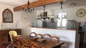 Un comedor con una mesa y sillas de madera, una araña y una cocina al fondo.