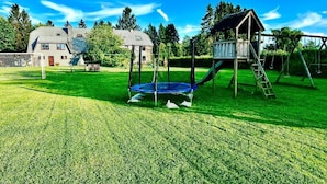 A playground with a trampoline and slide, surrounded by a well-maintained lawn and a house in the background. - Holiday Apartment in Beautiful Hunningen (Buellingen)