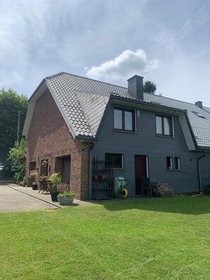 Une maison à deux étages, avec un toit en pente, une partie en briques et une façade grise.