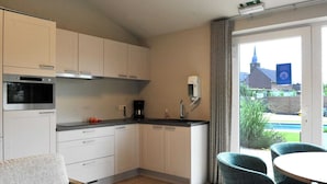 A modern kitchen with a built-in oven, a coffee machine, and a sink. There is a dining area with a round table and chairs. - Vlaanderen Cozy Cottage (Maasmechelen)