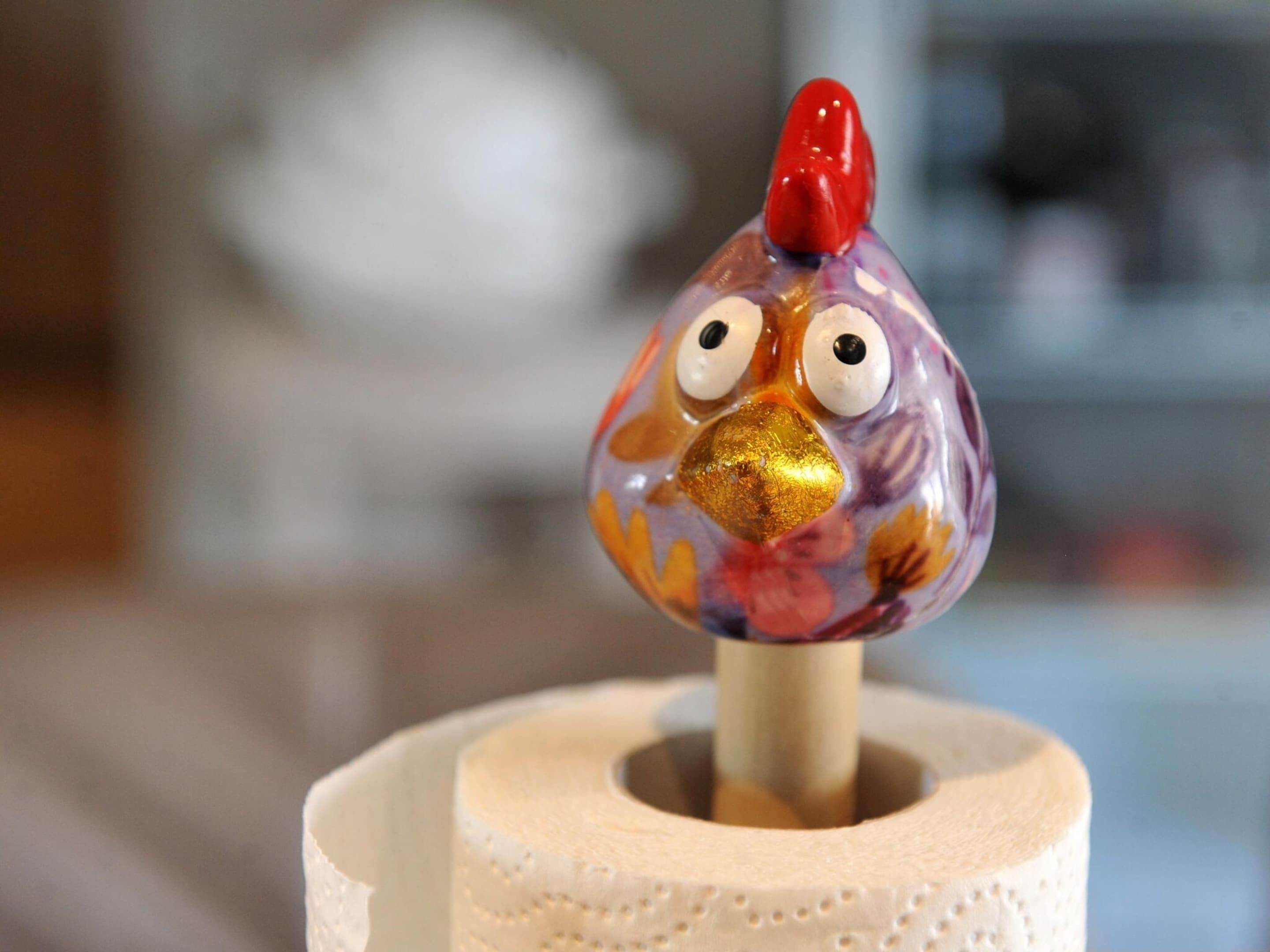 Ein dekoratives Objekt, das einen Vogel mit rotem Schnabel und großen, hervorstehenden Augen auf einem weißen, zylindrischen Gegenstand darstellt.