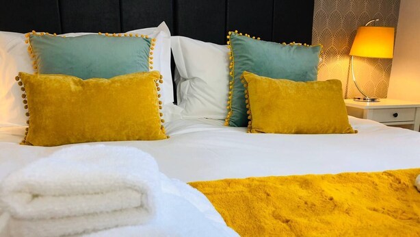 Ein ordentlich bezogenes Bett mit weißer und gelber Bettwäsche, zwei Kissen und ein gefaltetes weißes Handtuch.