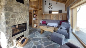 A cozy room with a stone fireplace, wooden beams, a sofa, and a bookshelf.