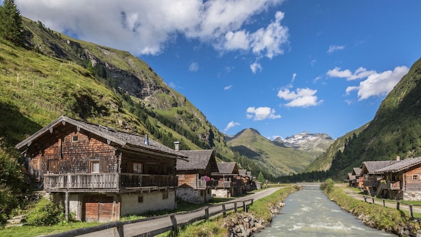 Una fila di case in legno con balconi lungo un fiume, circondate da montagne.