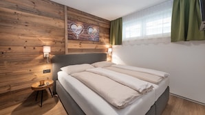 Camera da letto con parete in legno, letto con biancheria bianca, due lampade sui comodini e una tenda verde.